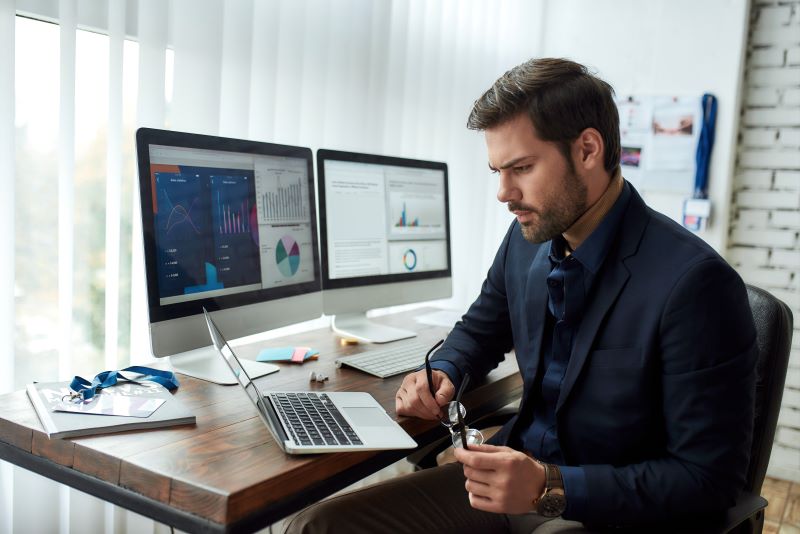Jovem empresário sentado em frente ao computador e analisando qual investimento empresarial deve fazer.